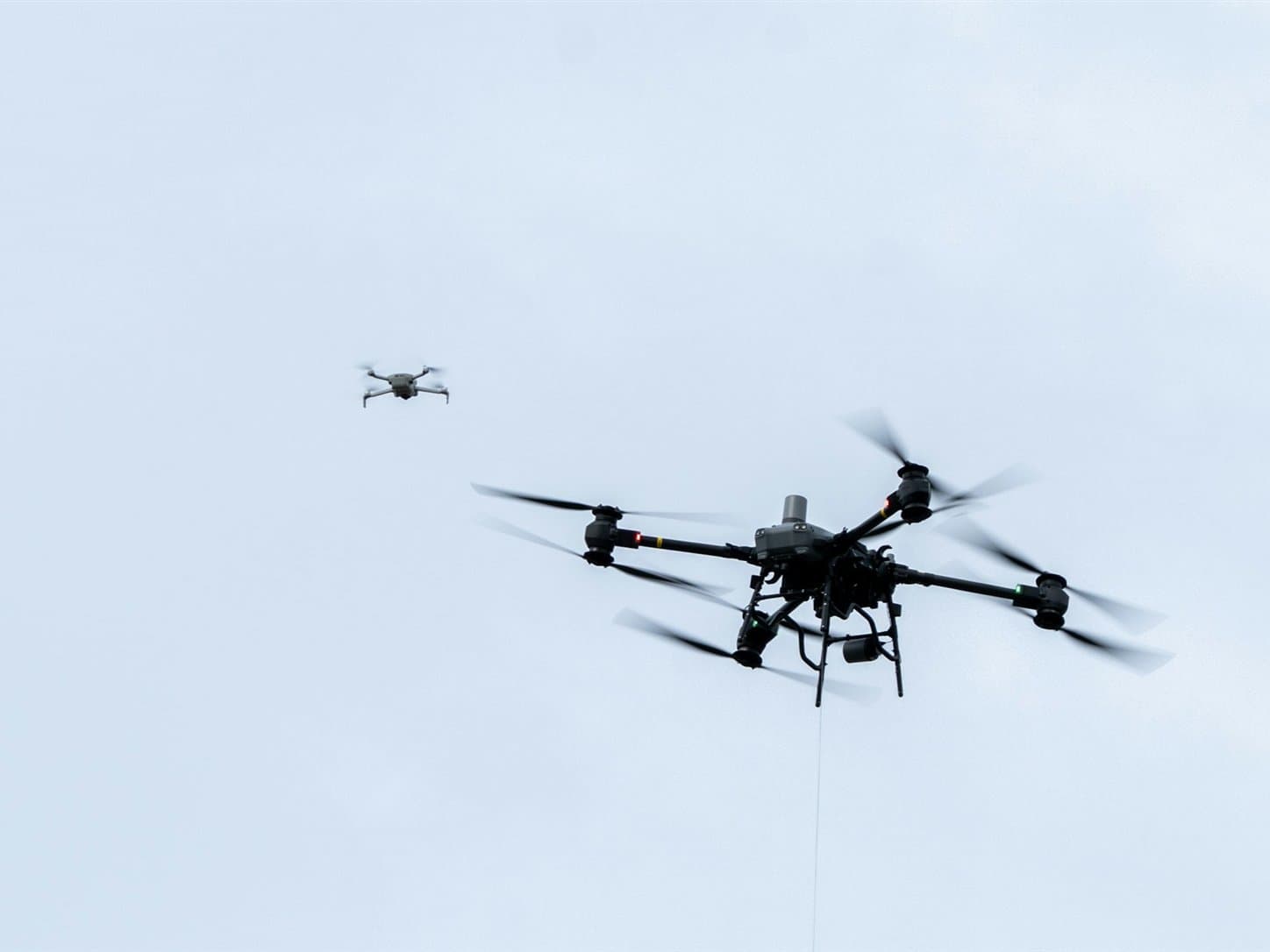 A sensor-equipped multirotor platform holding station in open sky while a second, smaller aircraft flies within the same airspace